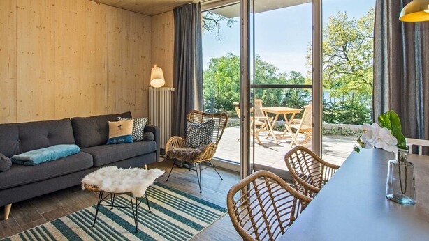 A modern living room with a sofa, chairs, a dining table, and a view through large windows. - "Söt Mine" Seaside Cottage – a stylish retreat on the Baltic Sea for up to 7 people (Loddin OT Stubbenfelde)