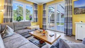 A modern living room with a sofa, coffee table, and a view of a garden through large windows.