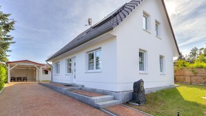 A white two-story house with a sloped roof, a covered patio, and a paved driveway.