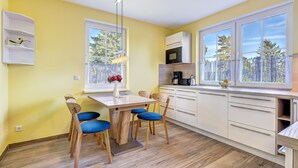 A modern kitchen with a dining area, large windows, and a view of trees.