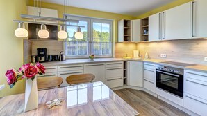 A modern kitchen with white cabinets, a built-in oven, and a dining area with a wooden table and chairs.