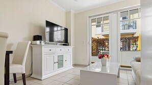 Een moderne woonkamer met een flatscreen televisie, witte kasten, een glazen salontafel en een bank.