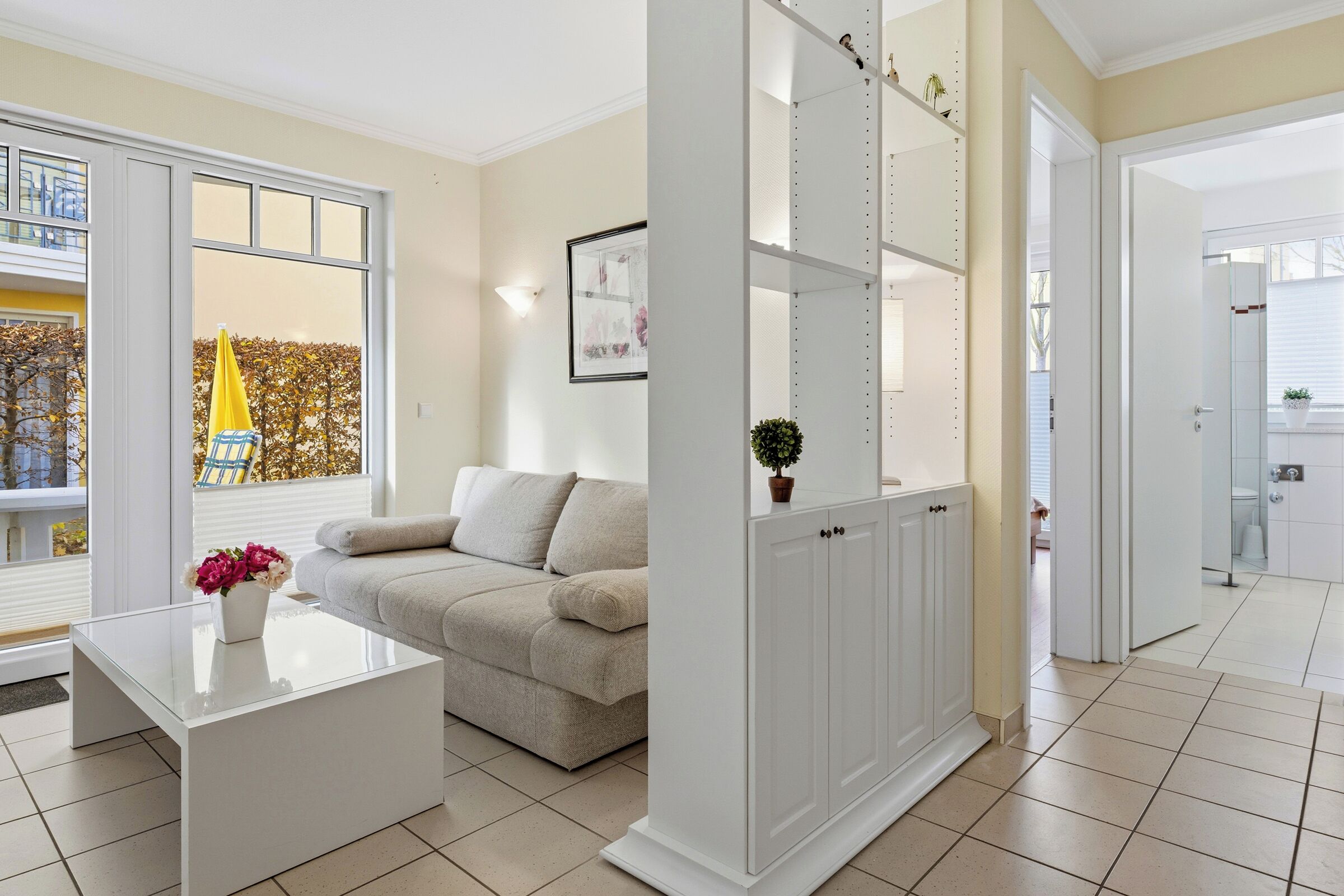 Una sala de estar moderna con una mesa de centro de vidrio, un sofá color crema y un mueble blanco con estantes.