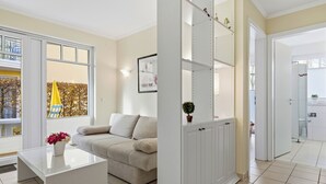 Een moderne woonkamer met een glazen salontafel, een beige bank en een witte kast met planken.