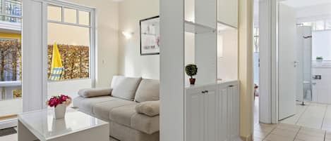 A modern living room with a glass coffee table, beige sofa, and a white cabinet with shelves.