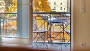 Parvekkeella on pöytä ja kaksi tuolia, ja sieltä on näkymä kadulle, jonka varrella kasvaa syksyisiä puita ja on rakennuksia.