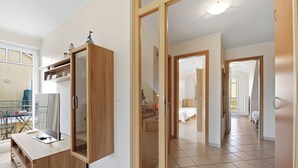 Een moderne keuken met een houten kastje en een glazen deur, een eethoek met een tafel en stoelen, en een gang die leidt naar een slaapkamer.