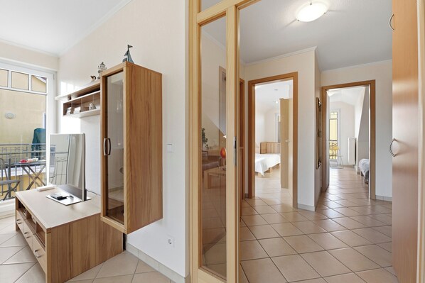 A modern kitchen with a wooden cabinet and a glass door, a dining area with a table and chairs, and a hallway leading to a bedroom.