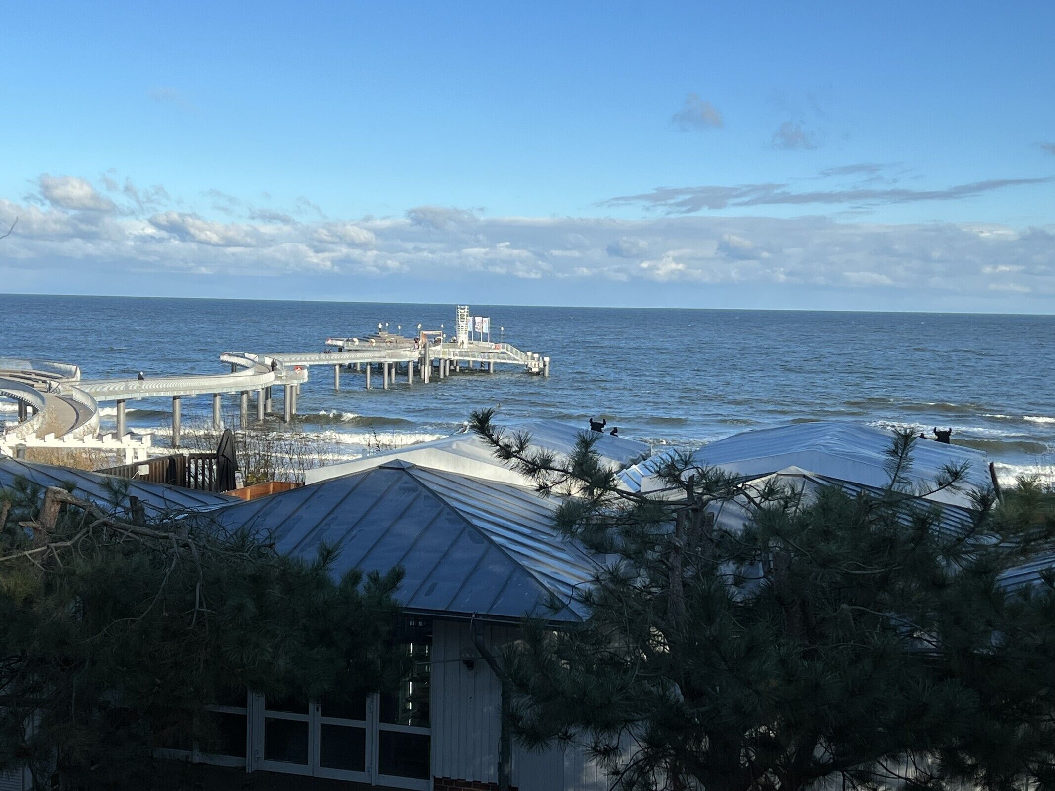 Une vue sur la côte, avec une jetée qui s’avance dans la mer, entourée d’immeubles et d’arbres.