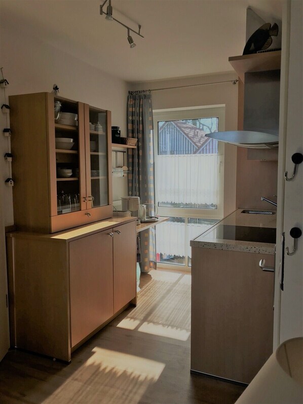 Cocina compacta con armarios de madera, estufa integrada y un amplio ventanal que proporciona luz natural.
