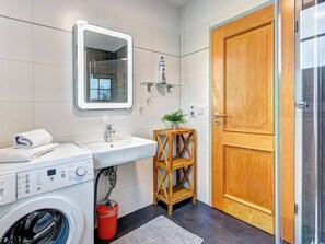 A modern bathroom with a washing machine, a sink, a mirror, and a wooden door. - Haus Sonnenschein, Whg. Leuchtfeuer: beach, balcony & WLAN for 5 persons (Trassenheide)