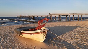 Un bote sobre una playa arenosa con un muelle al fondo.