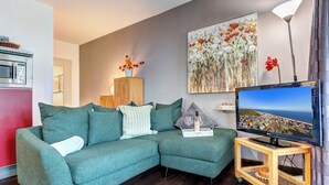 A living room with a green sectional sofa, a flat-screen TV, a wooden coffee table, and a painting on the wall.