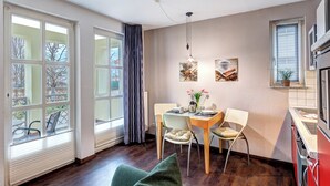 A dining area with a table set for two, chairs, a vase with flowers, and a window with curtains.