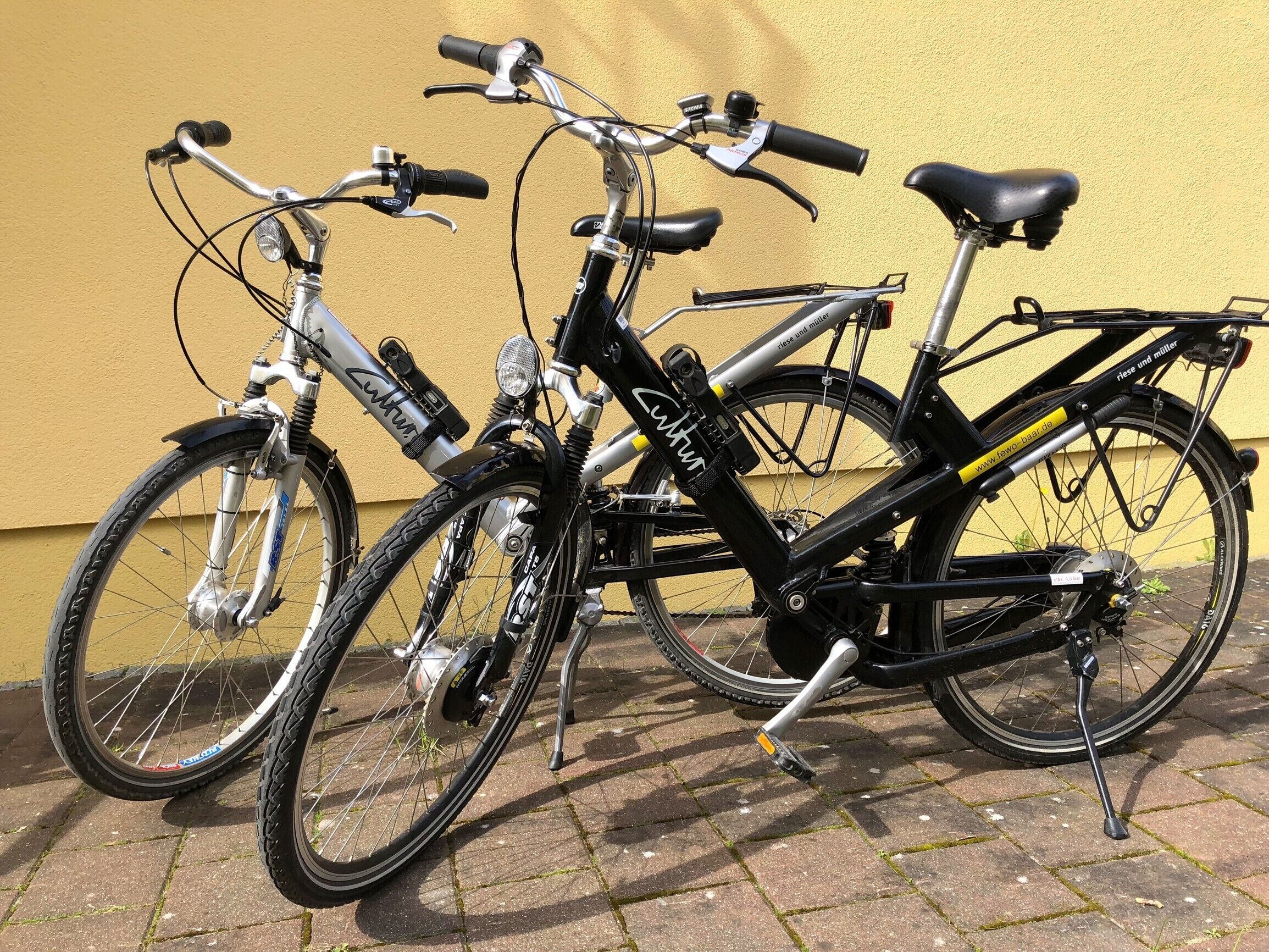 Två cyklar står parkerade mot en gul vägg.