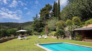 A swimming pool with a grassy area, lounge chairs, and a thatched-roof structure. - Charming Mediterranean villa with pool near Barcelona (Arenys de Munt)
