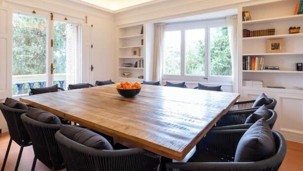 A dining area with a large wooden table surrounded by chairs, a bowl of fruit on the table, and bookshelves along the walls. - Charming Mediterranean villa with pool near Barcelona (Arenys de Munt)