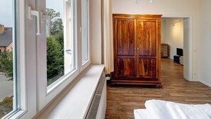 A hotel room with a large window, wooden wardrobe, and a radiator.