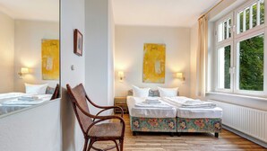 A hotel room with two beds, a chair, and large windows.