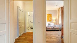 A hallway leading to a bedroom with a bed, a bathroom, and a painting on the wall.