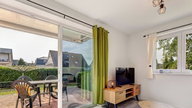 A modern living room with a sliding glass door leading to a patio, a wooden TV stand, and a small round table.