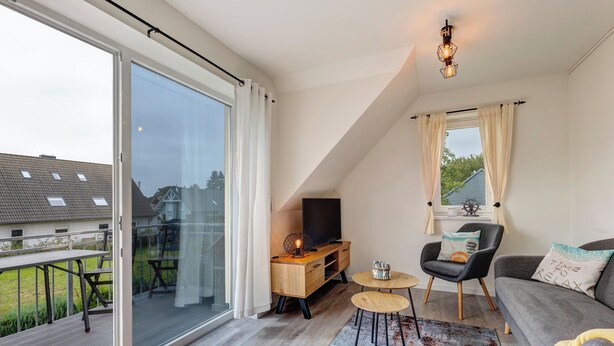A spacious living room with a large sliding glass door leading to a balcony, a cozy seating area with a sofa and armchairs, a small wooden table, and a television. - Vacation home Döhner Whg. 04 in Zinnowitz with balcony and 500 m to the sandy beach (Zinnowitz)