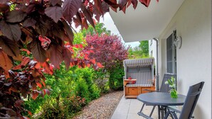 A patio with a table and chairs, a striped outdoor sofa, and a variety of plants and shrubs. - Residenz am Balmer See, apartment 46 with sauna & wellness by the lake (Balm)