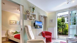 A modern living room with a sofa, a red armchair, a white armchair, a flat-screen TV, and a colorful rug. - Residenz am Balmer See, apartment 46 with sauna & wellness by the lake (Balm)