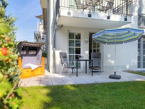 Een modern gebouw met twee verdiepingen, een balkon, een patio met een tafel en stoelen, en een gestreepte parasol.