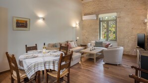 Un coin repas avec une table dressée pour quatre personnes, un canapé et un téléviseur, dans une pièce aux murs en pierre et au plancher en bois.
