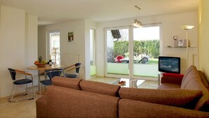 A modern living room with a sofa, a dining area with a table and chairs, a TV, and a balcony with a view of the outdoors. - House Vincent, apartment 1 in Zinnowitz: 62 m² for 4 with terrace and WLAN (Zinnowitz)