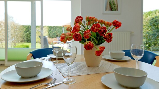 A dining table set with white bowls, wine glasses, and a vase of red flowers. - House Vincent, apartment 1 in Zinnowitz: 62 m² for 4 with terrace and WLAN (Zinnowitz)