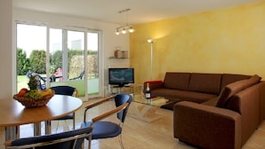 A living room with a brown sofa, a glass coffee table, a TV, and a dining area with a table and chairs. - House Vincent, apartment 1 in Zinnowitz: 62 m² for 4 with terrace and WLAN (Zinnowitz)