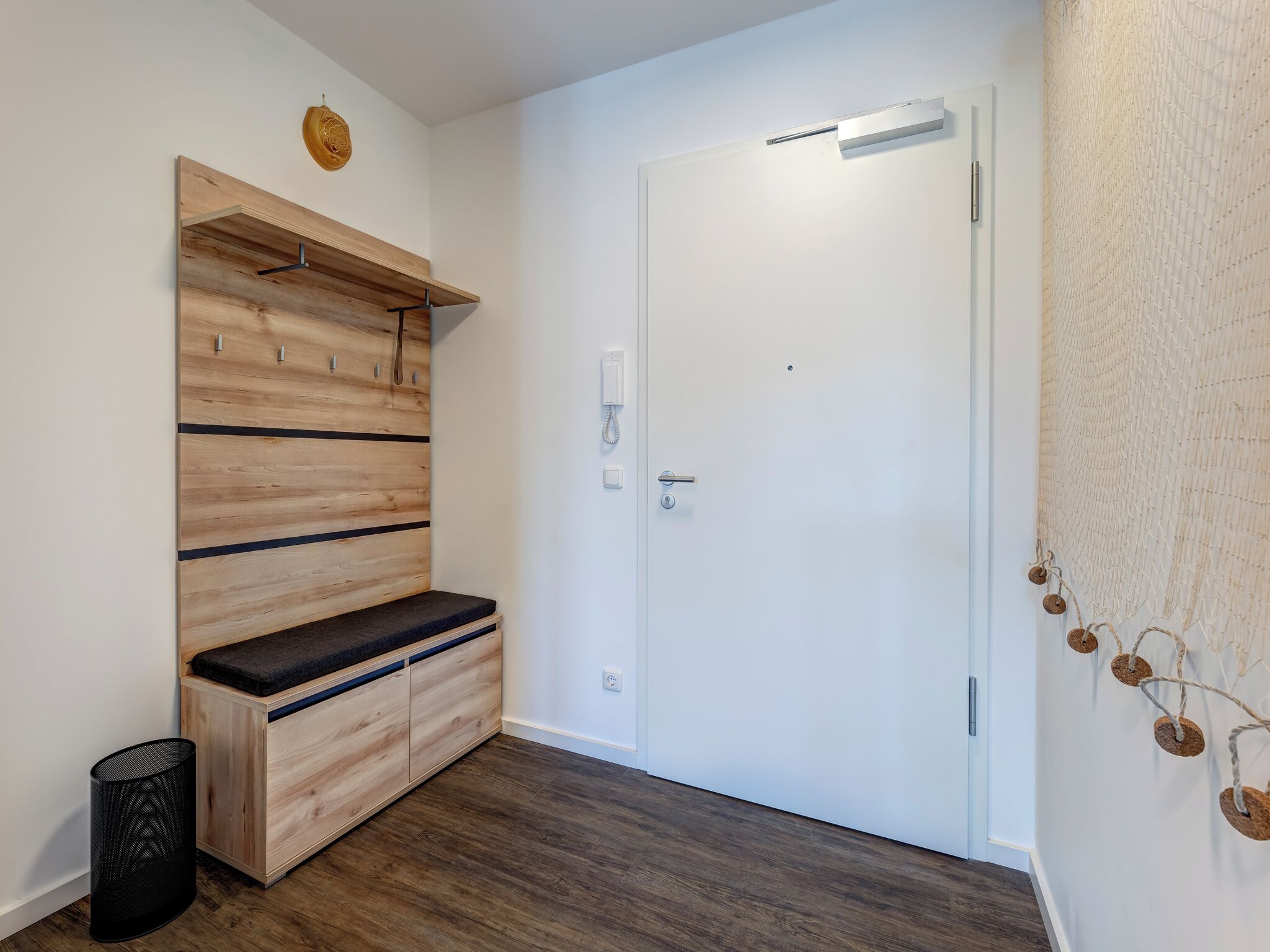 A hallway with a wooden bench, a white door, and a wall-mounted phone.