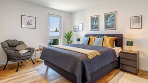 A modern bedroom with a large bed, a chair, and a nightstand. - Bernsteinquartier, Mister Bernstein, Whg. 01.08 in Kölpinsee - pure relaxation (Kölpinsee)