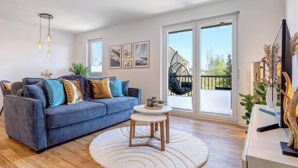 A modern living room with a blue sofa, a round coffee table, and a hanging chair by the large sliding glass doors. - Bernsteinquartier, Mister Bernstein, Whg. 01.08 in Kölpinsee - pure relaxation (Kölpinsee)