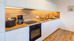A modern kitchen with white cabinets, a wooden countertop, a coffee maker, a toaster, and a sink. - Bernsteinquartier, Mister Bernstein, Whg. 01.08 in Kölpinsee - pure relaxation (Kölpinsee)