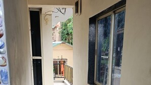 A corridor with a window on the right, a door at the end, and a tiled floor. - Golden Heaven (Mahabaleshwar)