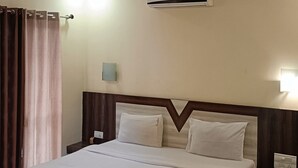A hotel room with a large bed, a ceiling fan, an air conditioning unit, a nightstand with a lamp, and a curtain. - Golden Heaven (Mahabaleshwar)