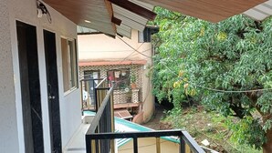 A covered balcony with a tiled floor, a wooden ceiling, and a view of a house with a tiled roof and potted plants. - Golden Heaven (Mahabaleshwar)