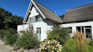 Una casa moderna amb façana blanca, teulada inclinada i un jardí ben cuidat amb diverses plantes i flors.