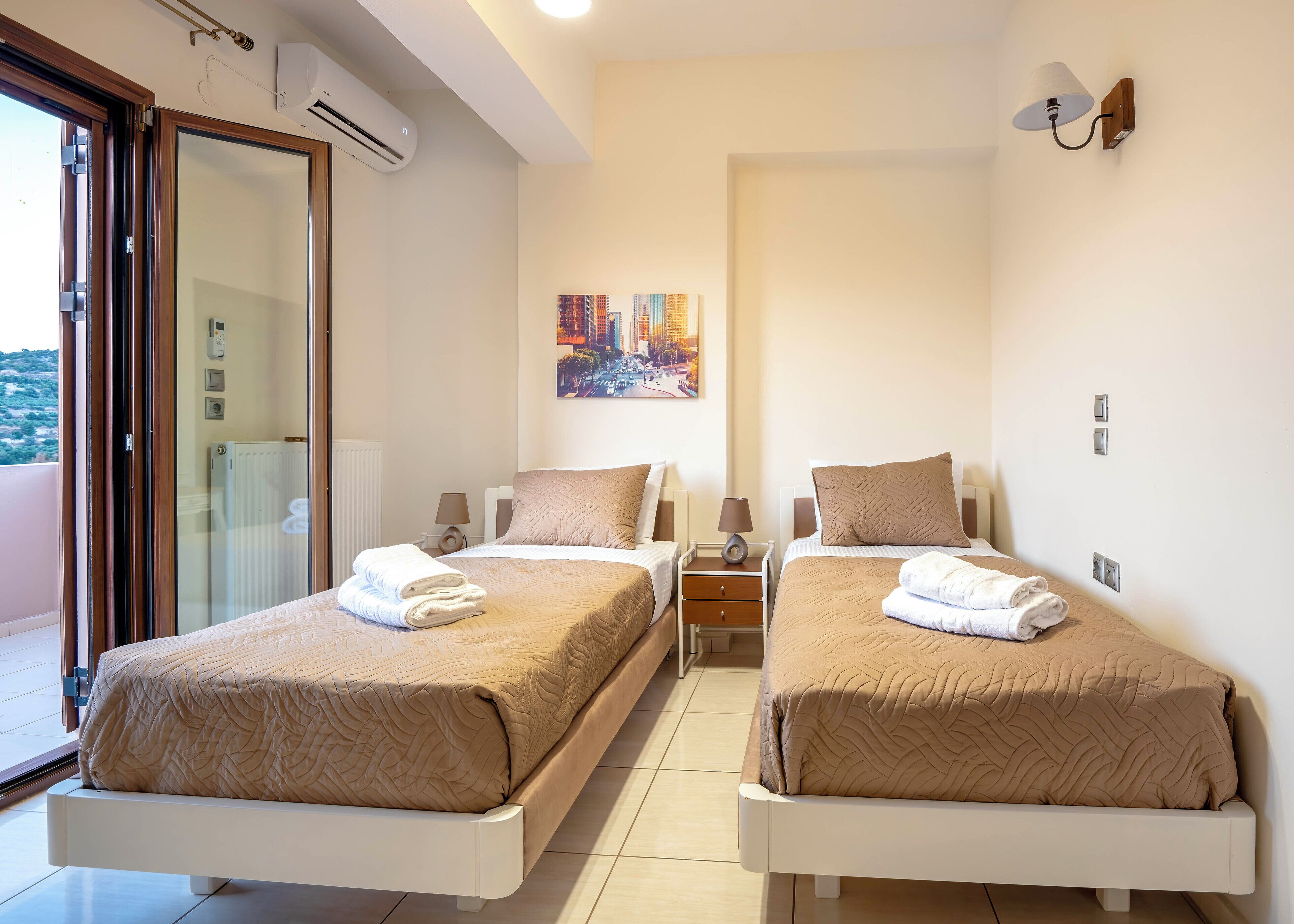 A hotel room with two beds, a balcony, and a painting on the wall.