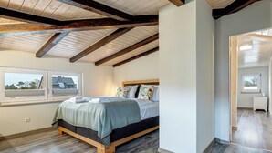A bedroom with a wooden ceiling, a bed with a floral pillow, and a window with a view of a house. - Vacation home Thorina in Bansin: 90 m² for 5, terrace & close to the beach 1 km (Bansin)