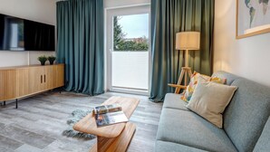 A modern living room with a grey sofa, wooden coffee table, and a TV on the wall. - Vacation home Thorina in Bansin: 90 m² for 5, terrace & close to the beach 1 km (Bansin)