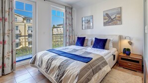 Une chambre à coucher avec un grand lit, une table de chevet, une lampe fixée au mur et une fenêtre avec des rideaux.