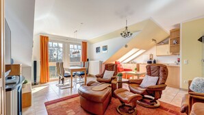 Un vaste espace de vie comprenant une table à manger, deux fauteuils en cuir inclinables, un tapis rouge et une cuisine à l’arrière-plan.