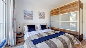 Une chambre à coucher avec un lit, une table de chevet, une commode et une fenêtre avec des rideaux.