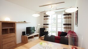 Moderni olohuone, jossa on puinen ruokapöytä, televisio ja viihtyisä oleskelualue, johon kuuluu punainen sohva ja musta nojatuoli.