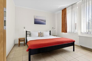 Un dormitorio con una cama, una mesita de noche, una lámpara de pared, una ventana con cortinas y un cuadro en la pared.