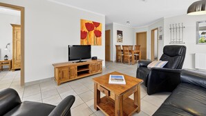 A living room with a TV, wooden furniture, a black leather sofa, and a dining area with wooden chairs.